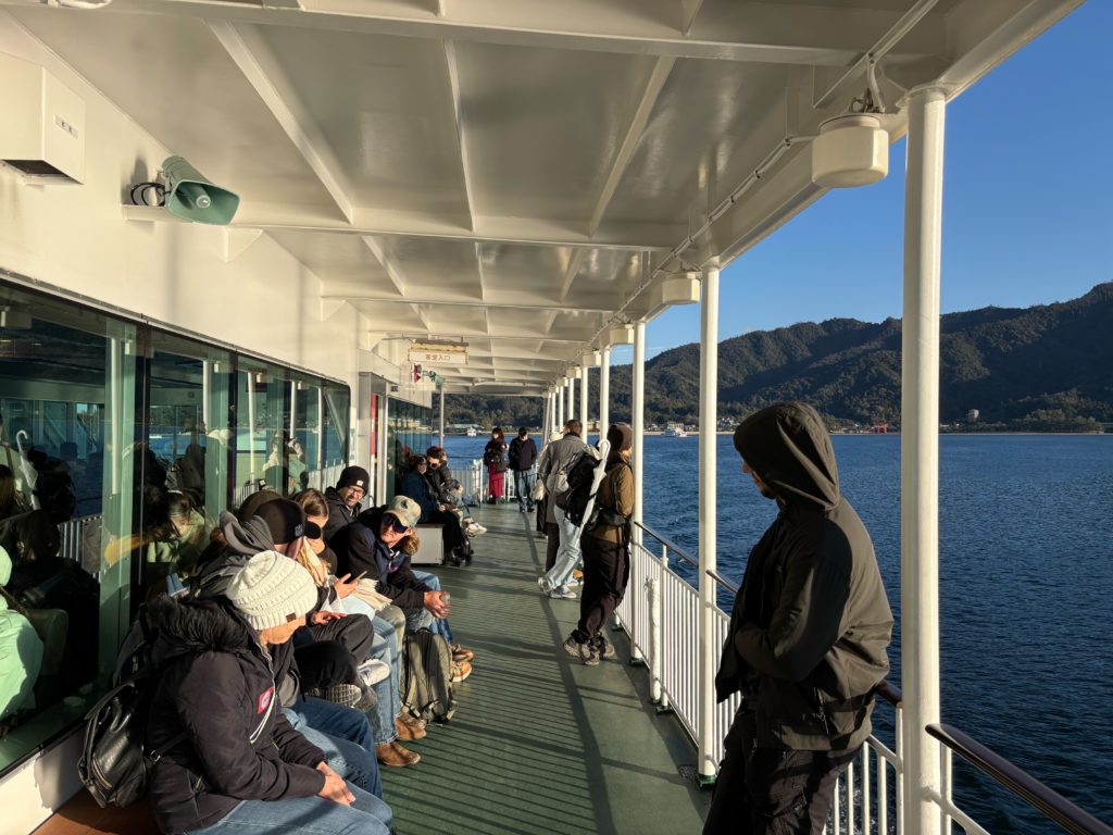 Passengers standing on the outdoor deck of Miyajima ferry enjoying views